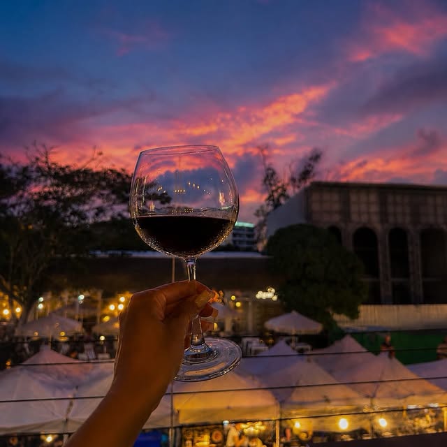 A glass of wine held against the sunset over the Boat Avenue night-market lights, taken from the SALTY terrace.